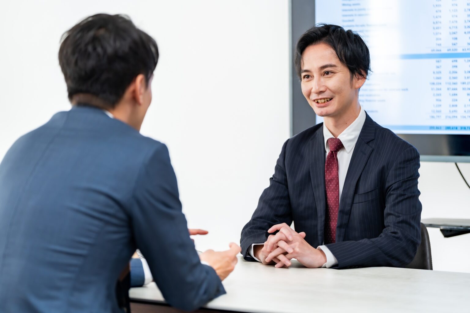 オフィスで机を挟んで対話するビジネスパーソン